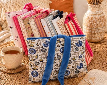 May include: A collection of rectangular fabric pouches featuring various patterns including floral, striped, and solid designs. The front-most pouch is white with a blue and yellow floral print and two long blue velvet ties hanging down the centre.