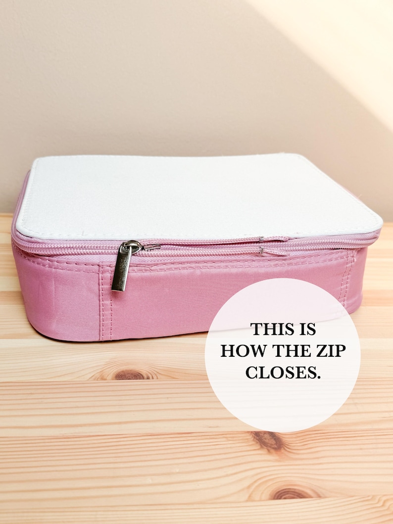 Puede incluir: Un estuche rectangular rosa con una parte superior blanca y un cierre de cremallera plateado. El texto "THIS IS HOW THE ZIP CLOSES" est&aacute; en un c&iacute;rculo blanco en el lado derecho de la imagen.