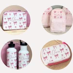 Puede incluir: Bolsa de almuerzo, mochila, botellas de agua y fiambrera rosas y blancas. Cada art&iacute;culo presenta un patr&oacute;n de lazos rosas y el nombre "Olivia" o "Hallie". La bolsa de almuerzo tiene un asa y la mochila tiene un bolsillo frontal.