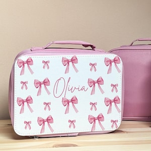 Puede incluir: Bolsa de almuerzo rosa con un panel frontal blanco con un patr&oacute;n de lazos rosas. El nombre "Olivia" est&aacute; escrito en cursiva. Una segunda bolsa rosa s&oacute;lida es visible en el fondo. La bolsa tiene un asa.