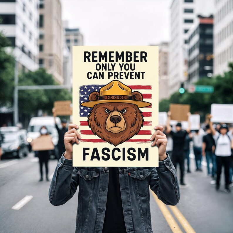 May include: A sign held up in a protest with the text "REMEMBER ONLY YOU CAN PREVENT FASCISM". The sign features a bear wearing a ranger hat in front of an American flag.