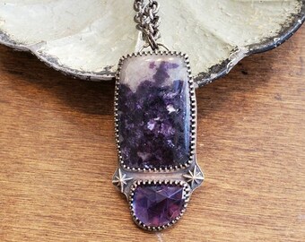 May include: A silver chain necklace with a purple and white stone pendant. The pendant is set in a silver frame with a smaller purple stone below it.