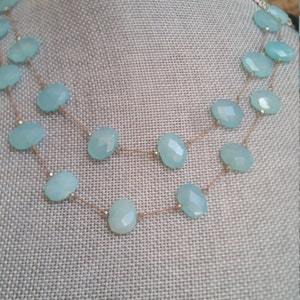 May include: A double-strand necklace with light blue gemstone beads and a thin gold chain.