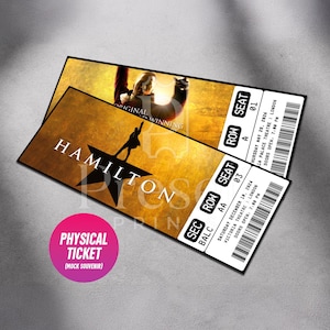 Puede incluir: Dos entradas rectangulares de recuerdo del musical Hamilton con fondo dorado, silueta de estrella negra y texto blanco. Las entradas muestran detalles del evento, incluyendo el Victoria Theatre, Londres, fechas, asientos y un c&oacute;digo de barras.