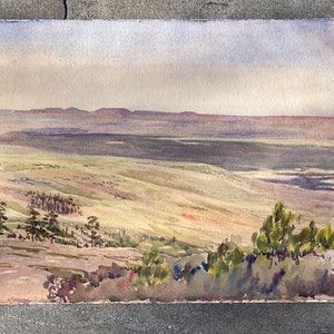May include: A watercolour painting depicting a landscape scene with rolling hills and a distant mountain range. The painting is done in shades of green, brown, and blue, with a hint of orange in the foreground. The sky is a pale blue with a few wispy clouds.