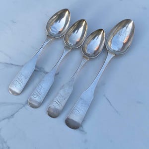 May include: Four silver spoons with ornate handles. Each spoon has a different engraved initial on the handle: "W.W", "W.W", "W.W", and "II".