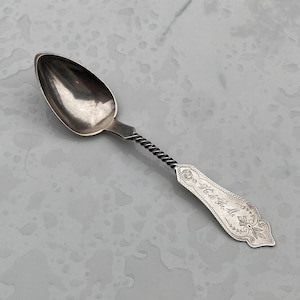 May include: A silver spoon with a twisted handle and an inscription that reads "A la de Dieu Au Nom de Dieu".