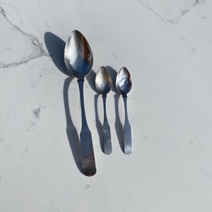 May include: Three silver spoons of varying sizes, arranged in order from largest to smallest.