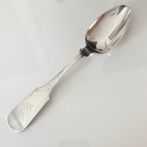 May include: A silver spoon with an ornate handle and a rounded bowl. The spoon has an inscription on the handle that reads "1801".