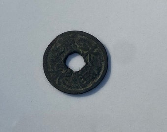 May include: A dark gray, round coin with a square hole in the center. The coin has intricate designs on both sides.