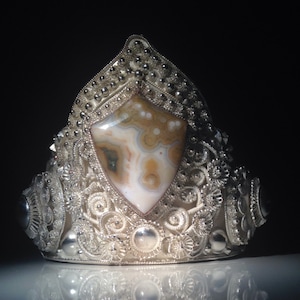 Puede incluir: Un anillo de plata con un diseño intrincado y una piedra de ágata blanca y marrón en el centro.