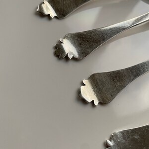 May include: Four silver spoons with ornate handles. The spoons are arranged in a row, with the handles pointing towards the top of the image.