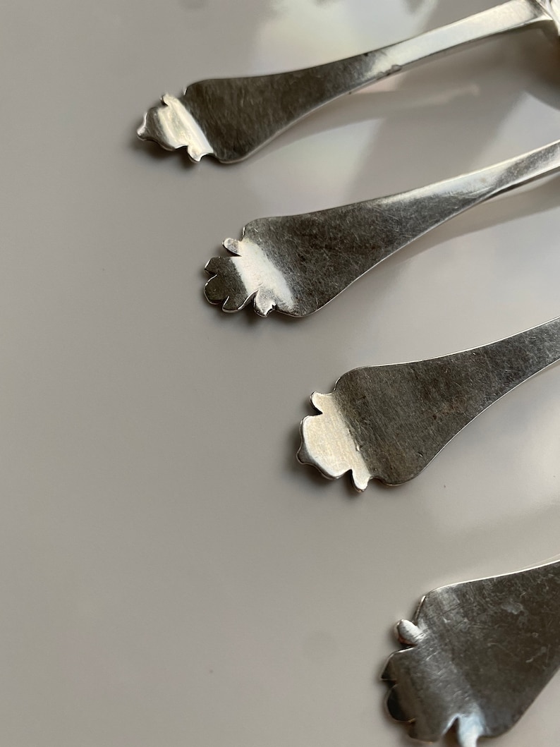May include: Four silver spoons with ornate handles. The spoons are arranged in a row, with the handles pointing towards the top of the image.