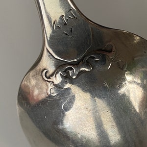 K&ouml;nnte beinhalten: Nahaufnahme der R&uuml;ckseite eines silbernen L&ouml;ffels mit der Inschrift "S.K.I.Y." und einem dekorativen Design.