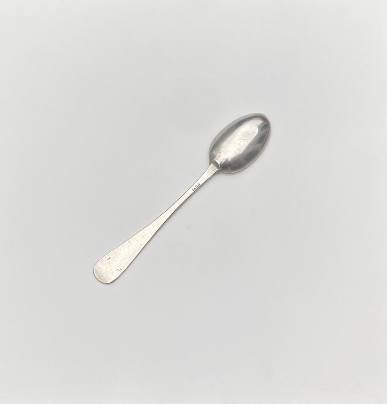 K&ouml;nnte beinhalten: Ein silberner Teel&ouml;ffel mit einer abgerundeten Schale und einem schlichten, eleganten Griff. Der L&ouml;ffel hat eine Punze auf der R&uuml;ckseite des Griffs.
