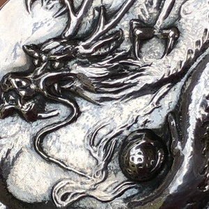 May include: A silver-toned metal belt buckle with a detailed dragon design. The dragon is holding a golf ball in its claws.
