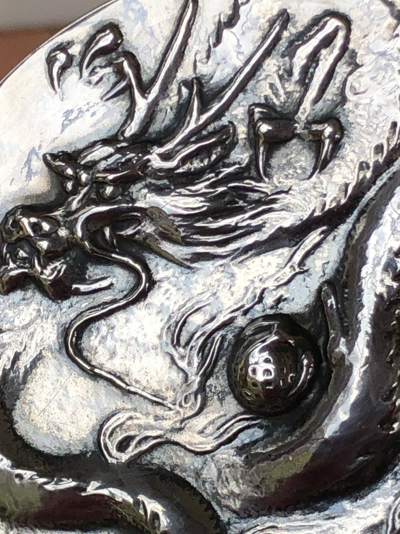 May include: A silver-toned metal belt buckle with a detailed dragon design. The dragon is holding a golf ball in its claws.