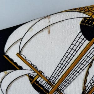 Puede incluir: Primer plano de un pa&ntilde;uelo de seda estampado con un dise&ntilde;o de velero. El pa&ntilde;uelo tiene un fondo blanco con detalles en negro y dorado. Las velas del barco son blancas y el aparejo es negro.