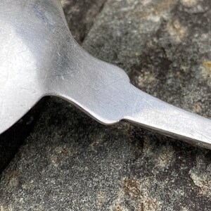 May include: Close-up of the back of a silver spoon with a worn, textured surface.