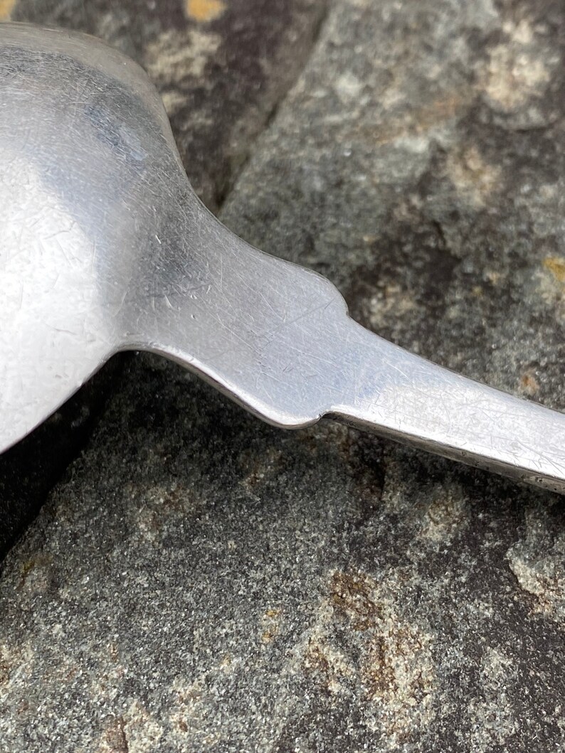 May include: Close-up of the back of a silver spoon with a worn, textured surface.