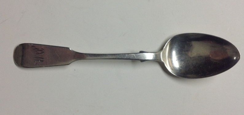 Puede incluir: Una cuchara de plata con un cuenco redondeado y un mango largo y delgado. El mango est&aacute; grabado con la palabra "JOHN".