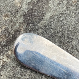 May include: Close-up of the rounded end of a silver spoon. The spoon is smooth and shiny, with a few scratches visible.