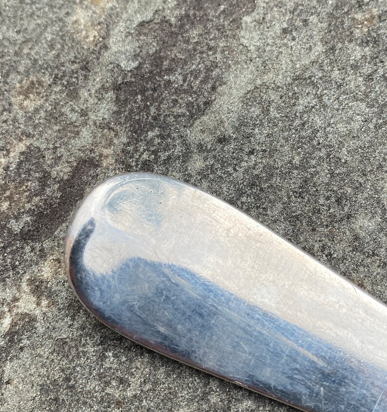 May include: Close-up of the rounded end of a silver spoon. The spoon is smooth and shiny, with a few scratches visible.
