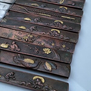 K&ouml;nnte beinhalten: Ein Satz von 10 japanischen Messern mit aufwendigen Designs auf den Griffen. Die Griffe sind aus dunklem Metall mit goldenen Akzenten. Die Designs beinhalten V&ouml;gel, Blumen und andere traditionelle japanische Motive.