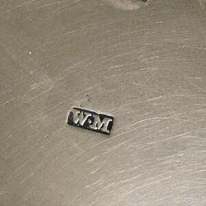 以下が含まれることがあります： 金属製の物体の銀の刻印のクローズアップ。刻印は「W.M.」です