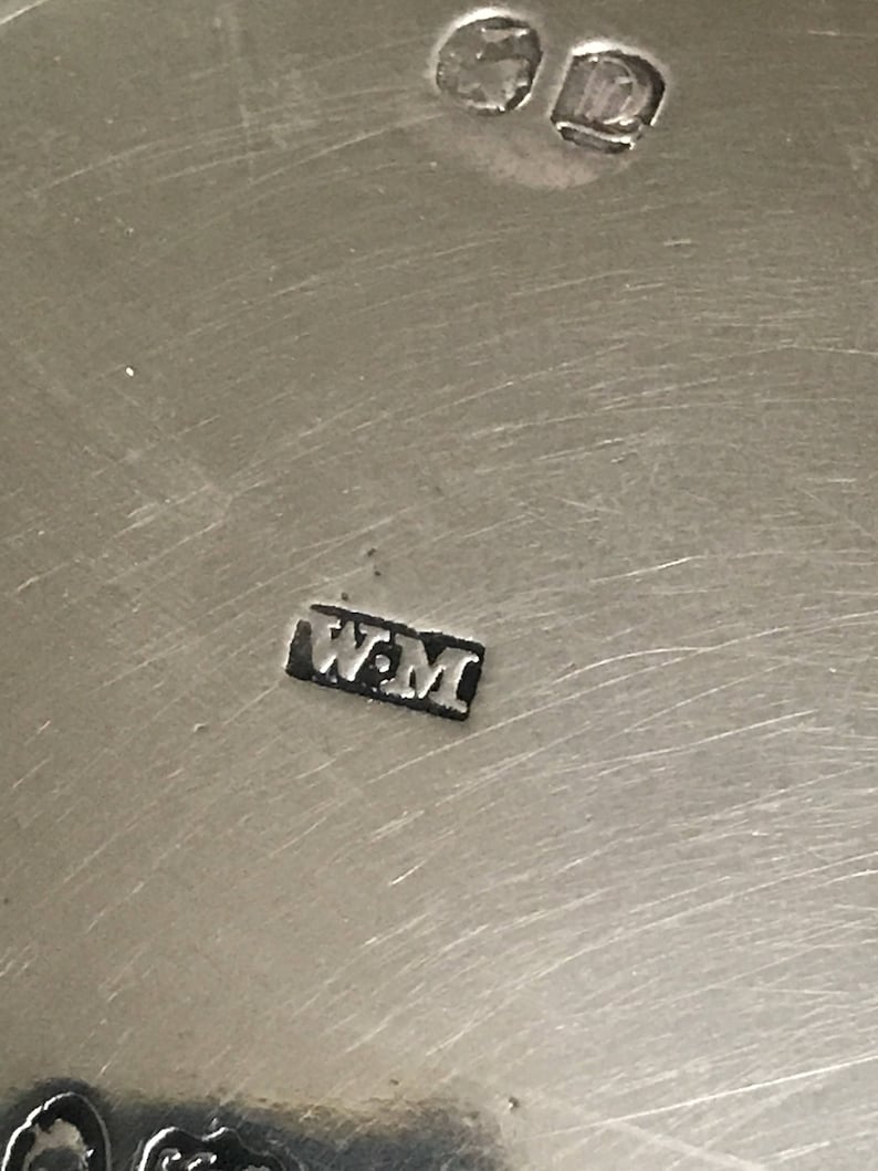 以下が含まれることがあります： 金属製の物体の銀の刻印のクローズアップ。刻印は「W.M.」です