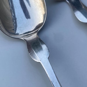 May include: Two silver spoons with ornate handles. The spoons are polished and reflect light.