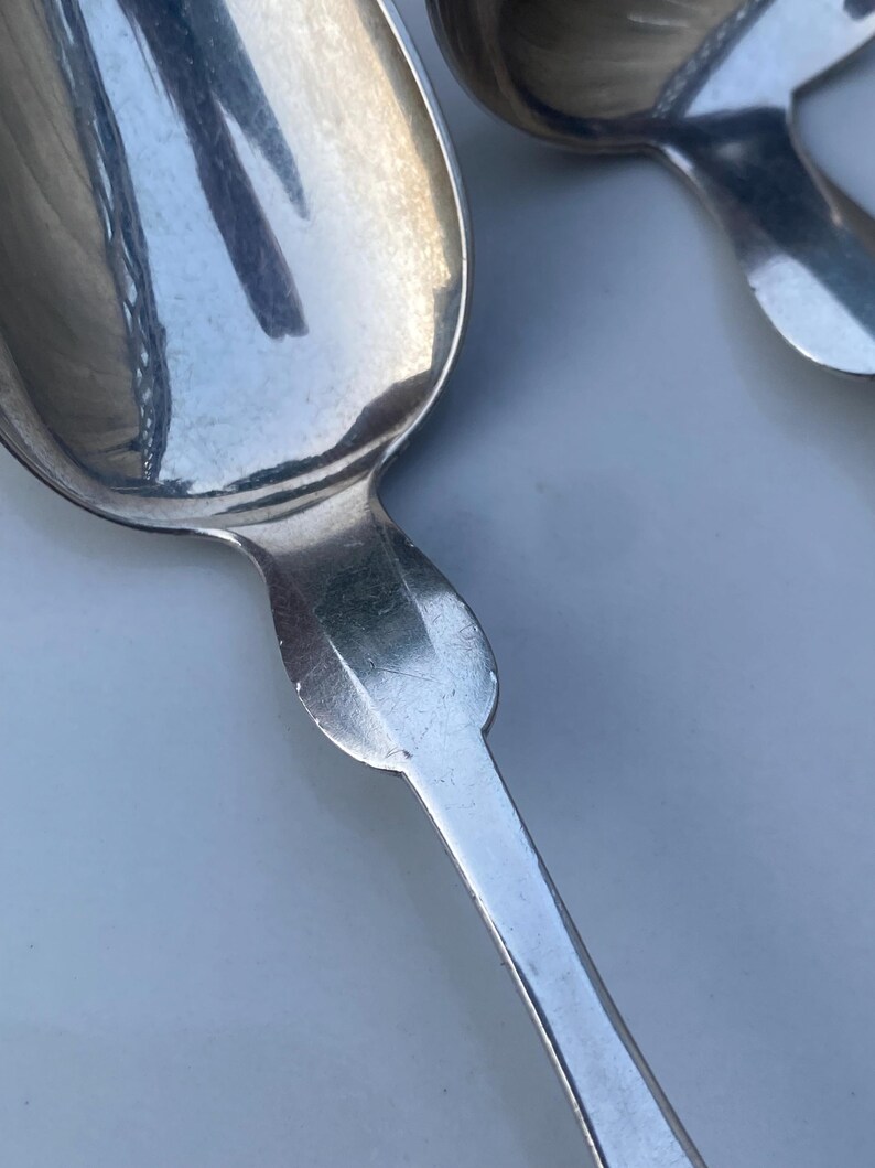 May include: Two silver spoons with ornate handles. The spoons are polished and reflect light.