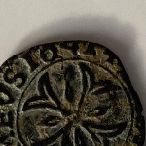 May include: Close-up of a circular, bronze-coloured coin with a five-pointed star design in the centre. The coin has a raised rim with lettering around the edge.