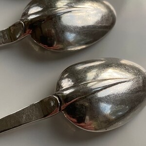 May include: Three silver spoons with ornate handles. The spoons are arranged in a row, with the handles pointing towards the right side of the image.