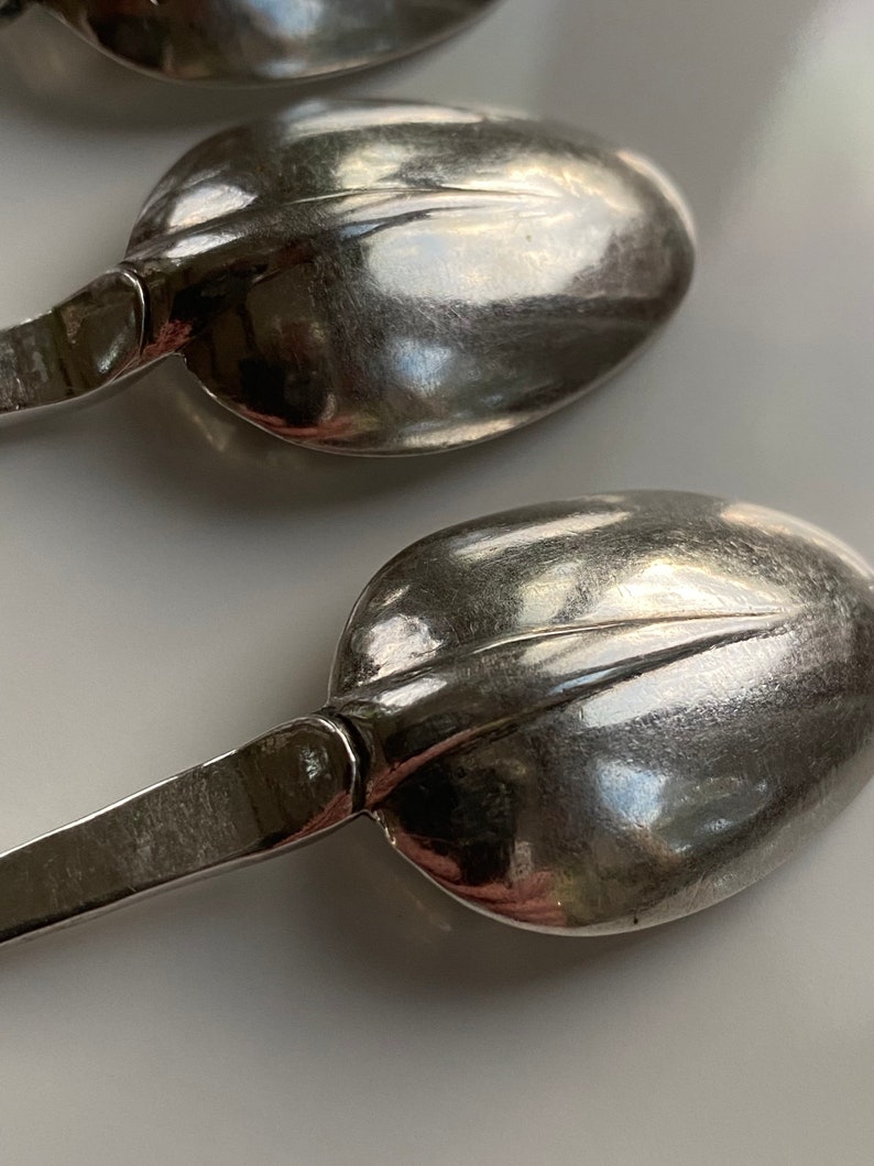 May include: Three silver spoons with ornate handles. The spoons are arranged in a row, with the handles pointing towards the right side of the image.