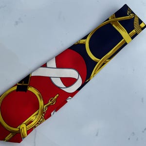 Puede incluir: Corbata de seda con dise&ntilde;o ecuestre rojo, azul marino y dorado. La corbata presenta un patr&oacute;n repetido de bocados de caballo dorados, cadenas y un dise&ntilde;o de cinta blanca sobre un fondo rojo y azul marino.