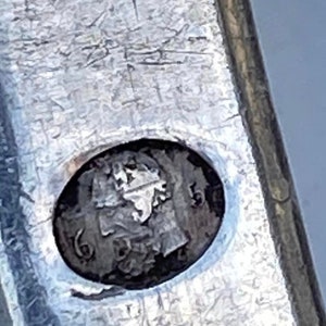 May include: Close-up of a silver object with a circular mark. The mark is a profile of a person's head with the number "16" visible.