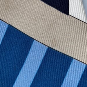 Puede incluir: Primer plano de un pa&ntilde;uelo de seda con un dise&ntilde;o geom&eacute;trico. El pa&ntilde;uelo presenta una combinaci&oacute;n de colores azul, azul claro, beige y azul marino. Rayas diagonales y formas rectangulares crean un patr&oacute;n moderno.