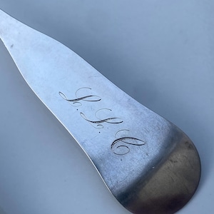 May include: Close-up of a silver spoon with the engraved initials "S.B." on the back.
