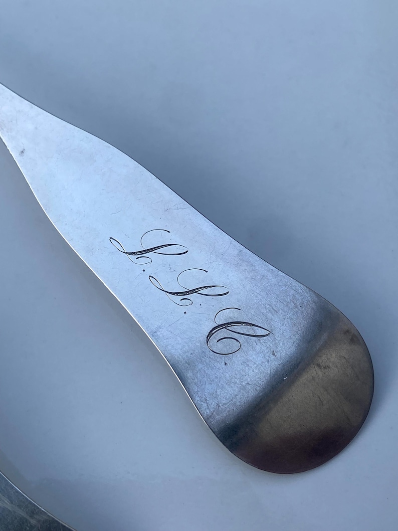 May include: Close-up of a silver spoon with the engraved initials "S.B." on the back.