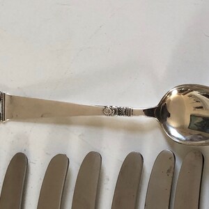 Puede incluir: Un juego de cubiertos, que incluye una cuchara de plata y varios cuchillos de plata. La cuchara tiene un mango adornado con un dise&ntilde;o floral.