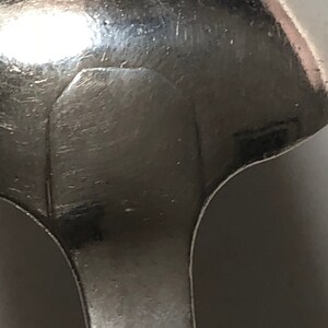 Puede incluir: Primer plano de la parte posterior de una cuchara de plata con una inscripci&oacute;n tenue.