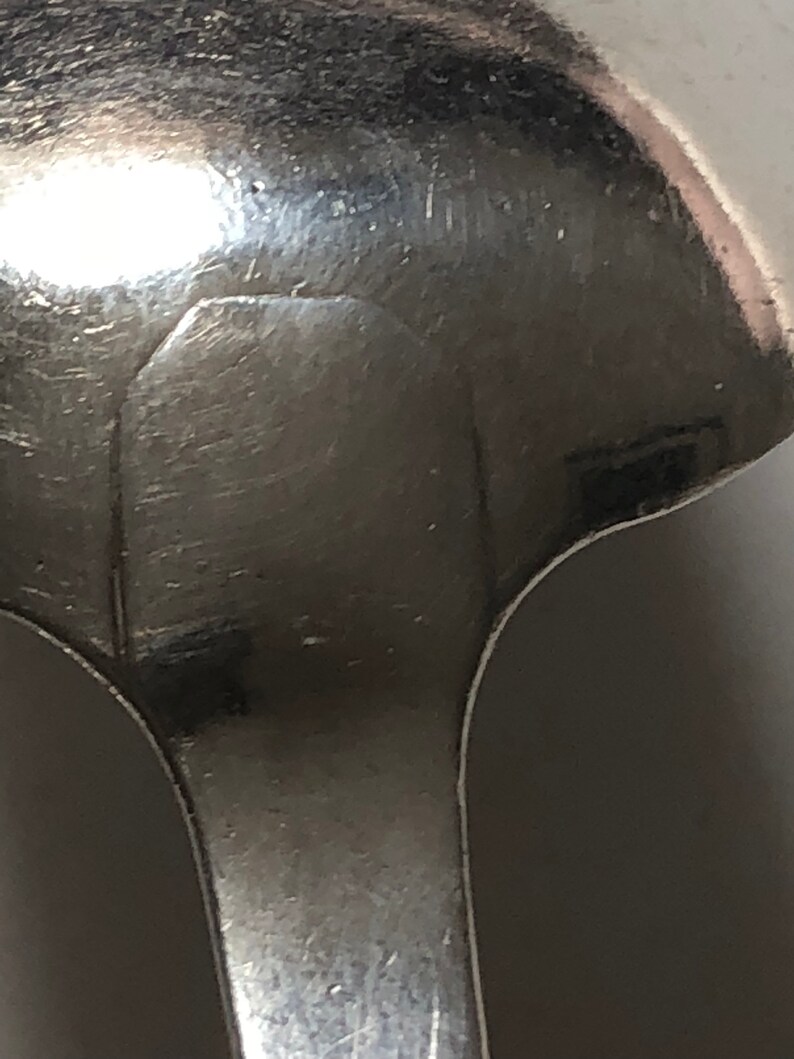 Puede incluir: Primer plano de la parte posterior de una cuchara de plata con una inscripci&oacute;n tenue.