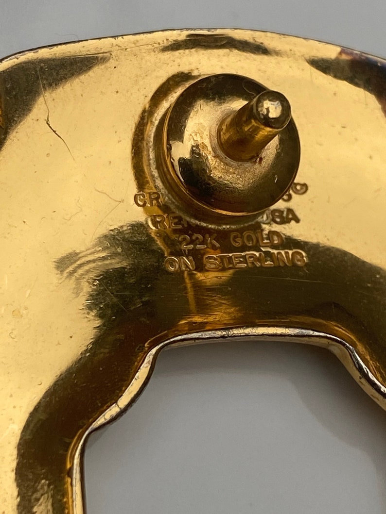 May include: Close-up of a gold-toned metal buckle with the text "22K GOLD ON STERLING" engraved on the back.