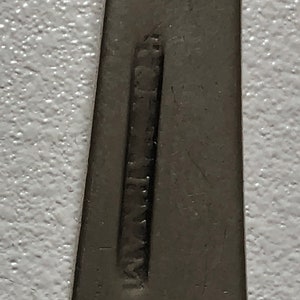 Puede incluir: Primer plano de un utensilio plateado con la palabra "Stainless" estampada en la parte posterior.