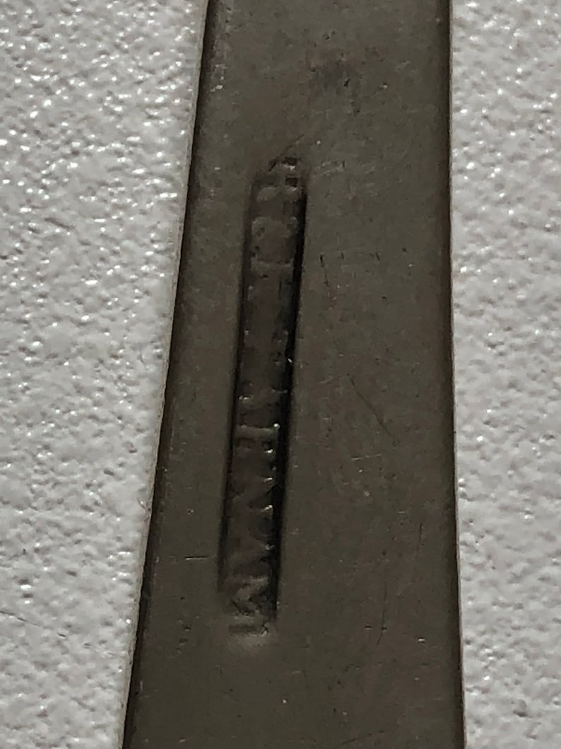 Puede incluir: Primer plano de un utensilio plateado con la palabra "Stainless" estampada en la parte posterior.