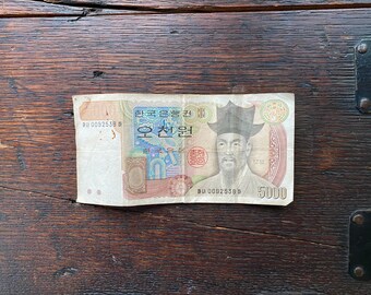Könnte beinhalten: Ein südkoreanischer 5.000-Won-Banknote mit einem Porträt von Yi Sun-sin, einem berühmten Admiral, mit dem Text "대한민국" (Republik Korea) und "오천원" (5.000 Won) darauf gedruckt.