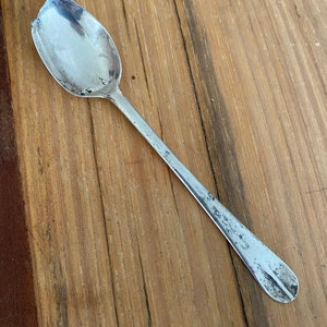 May include: A silver teaspoon with a rounded bowl and a long, slender handle. The spoon has a worn, antique look.