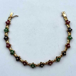 May include: A gold-toned bracelet featuring a floral design with red, green, and black gemstones. The bracelet has a woven gold chain and a clasp closure. The gemstones are arranged in a flower pattern.