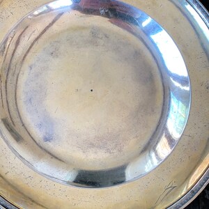 Puede incluir: Un plato de plata con un borde decorativo y una peque&ntilde;a marca en el centro.